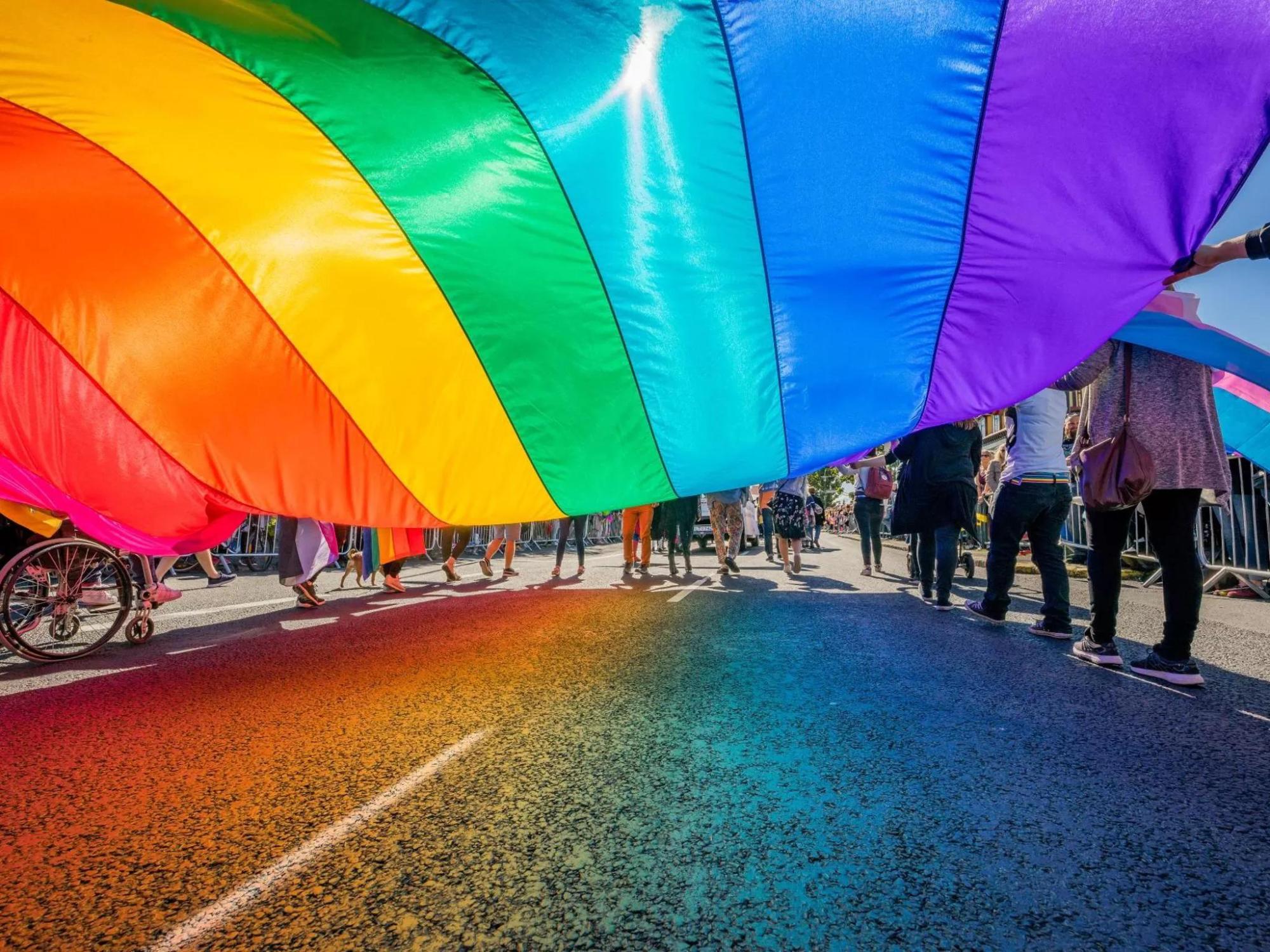People walking beneath a rainbow Pride flag.