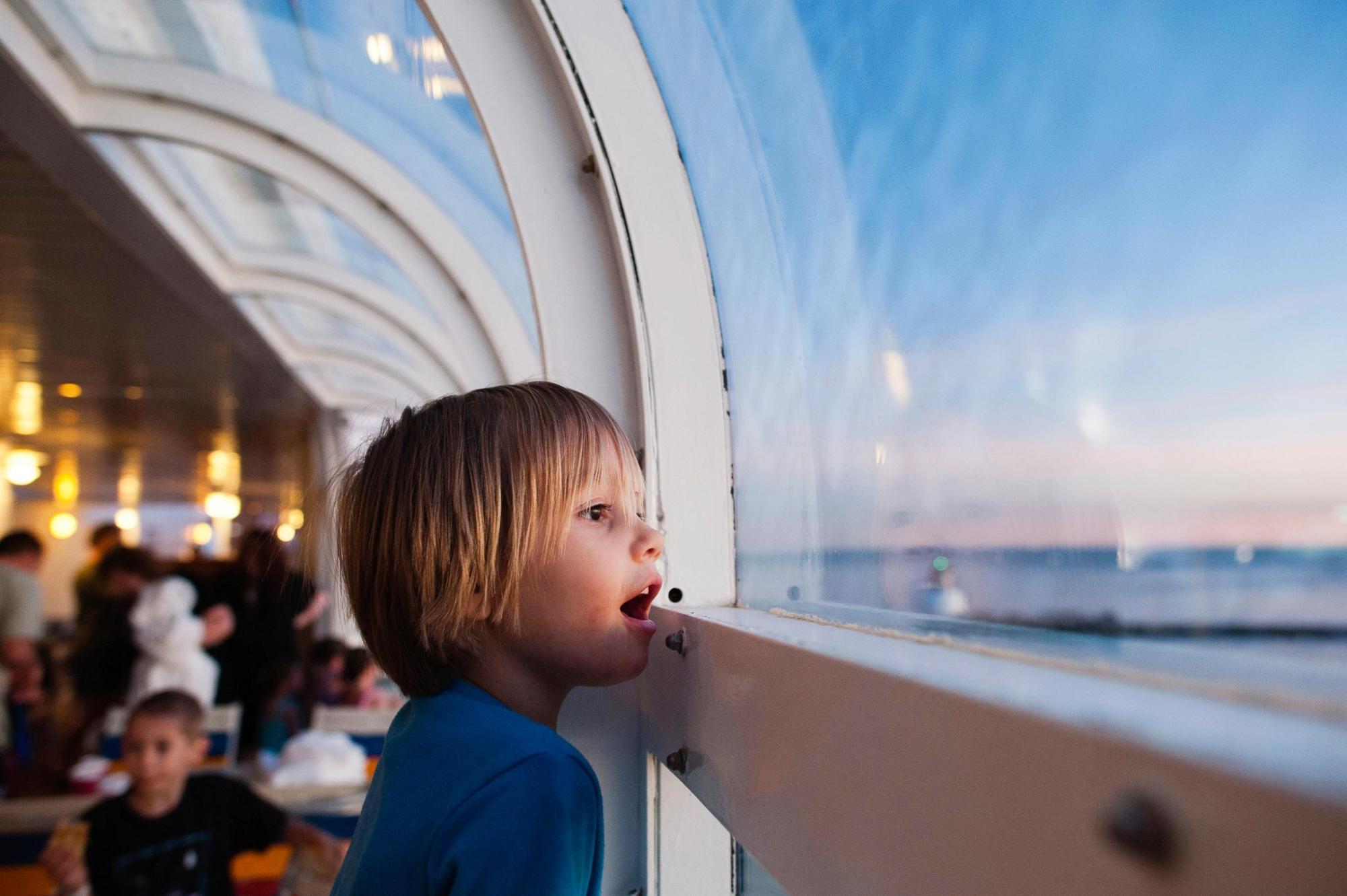 A child peers in awe from the window of a cruise