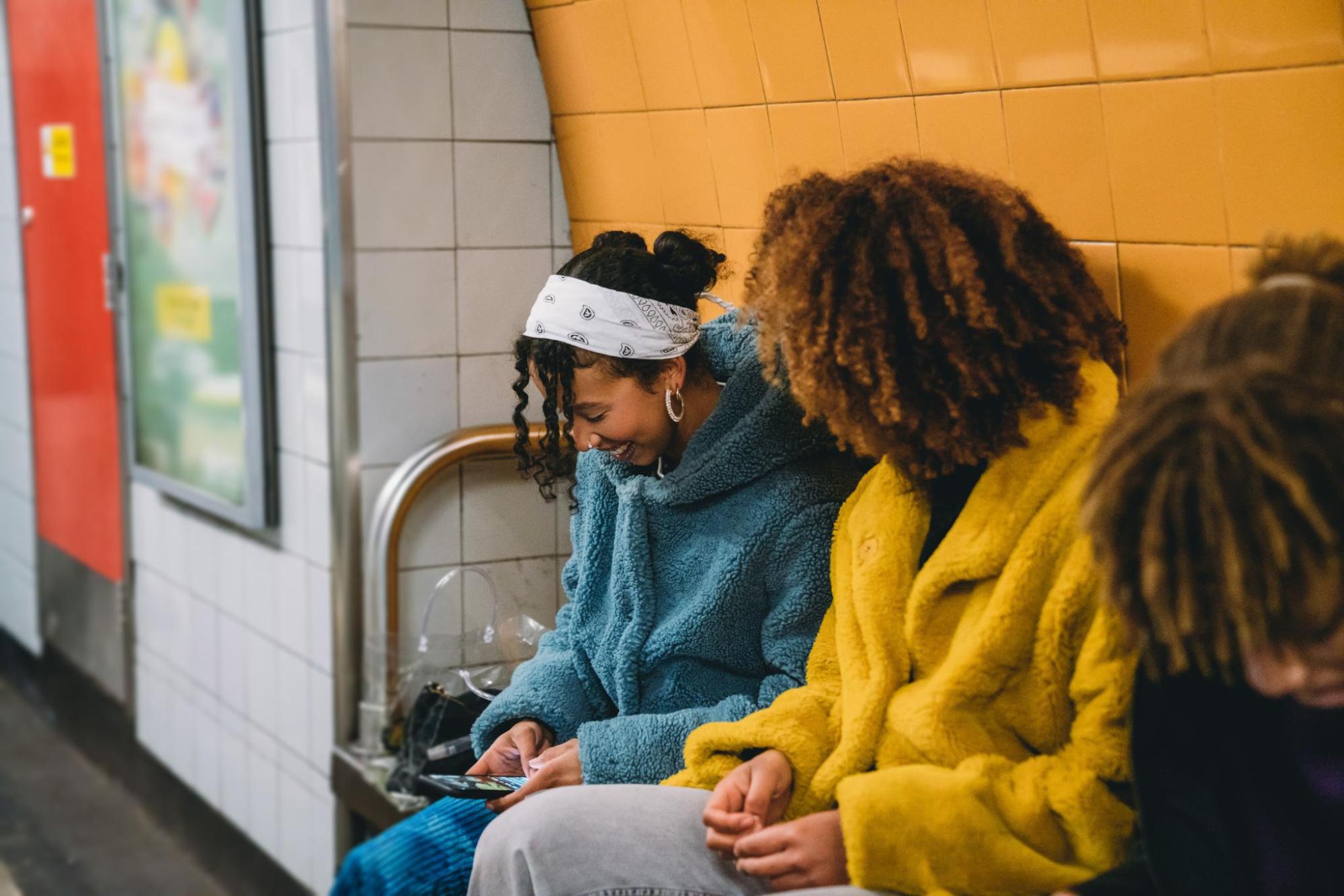 Three young girls sitting together in a subway station.