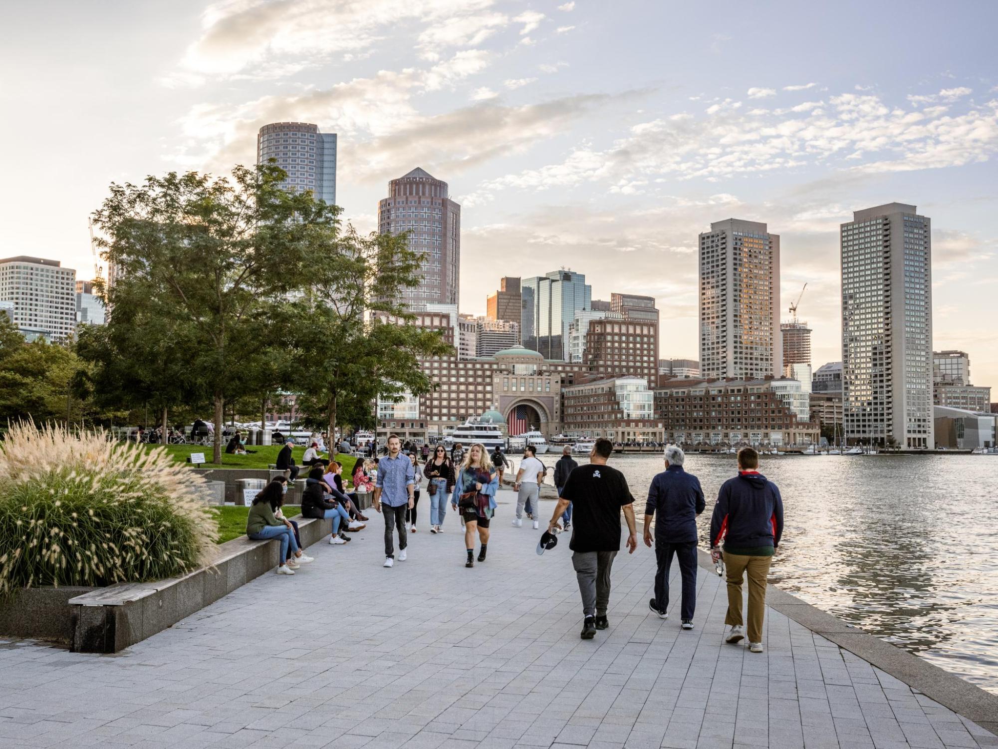 People stroll Boston's waterfront, the skyline is behind