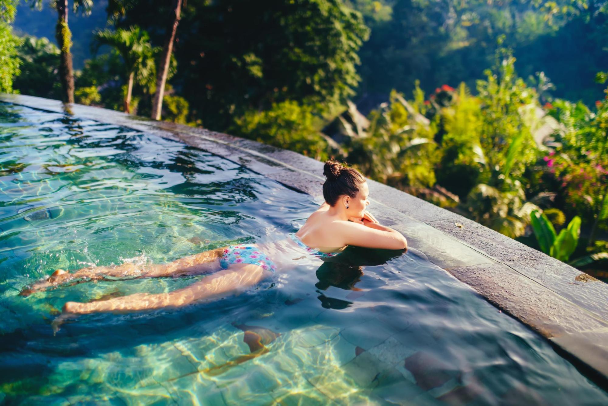 Woman floating in infinity pool surrounded by nature.