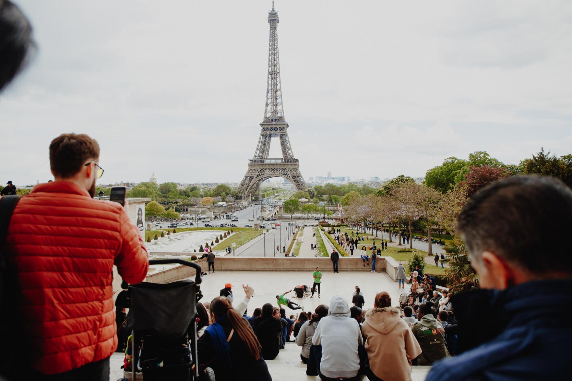 A man in a red jacket takes a picture by the Eiffel Tower