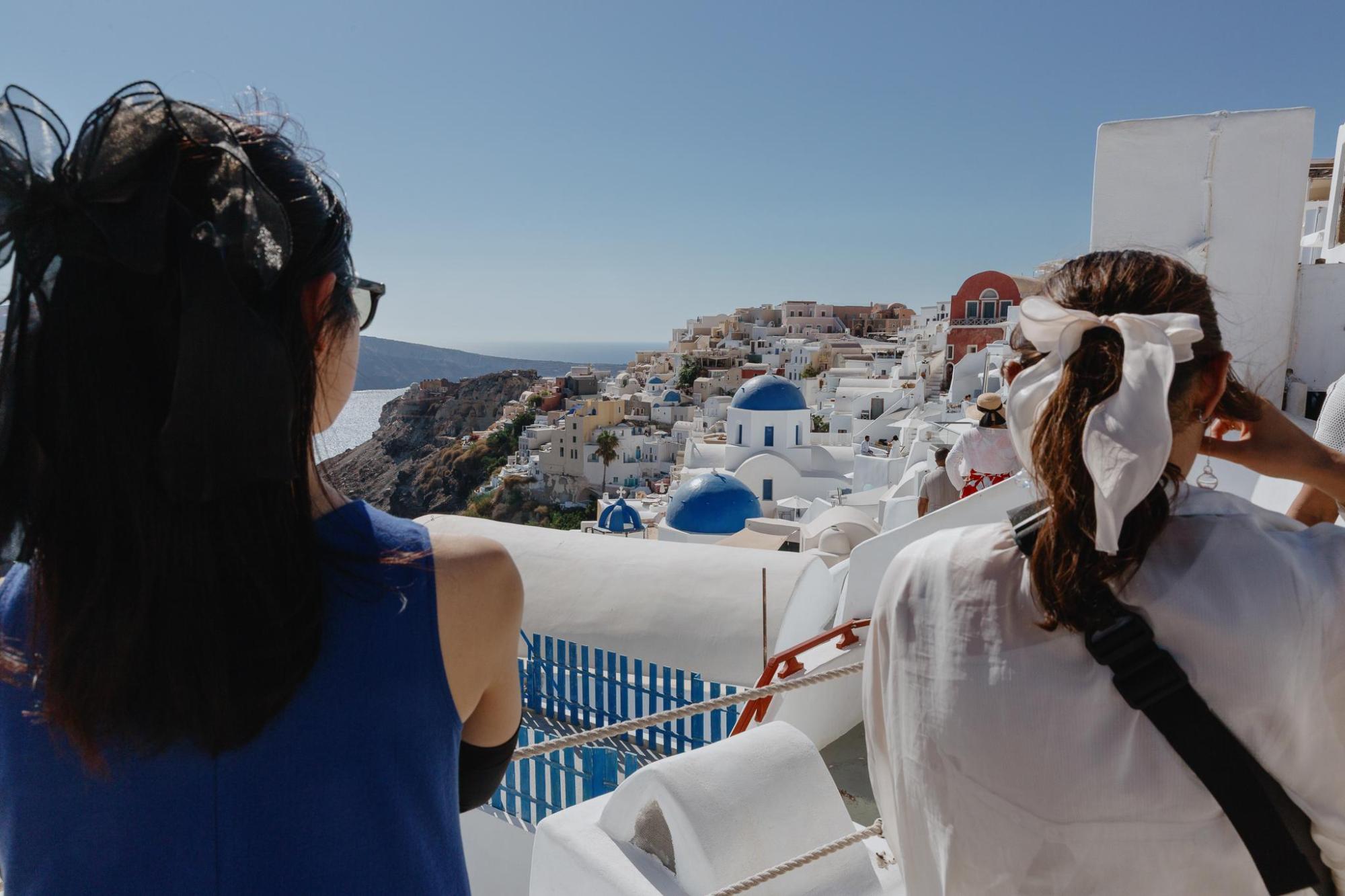 Two women overlooking Santorini’s white and blue domes