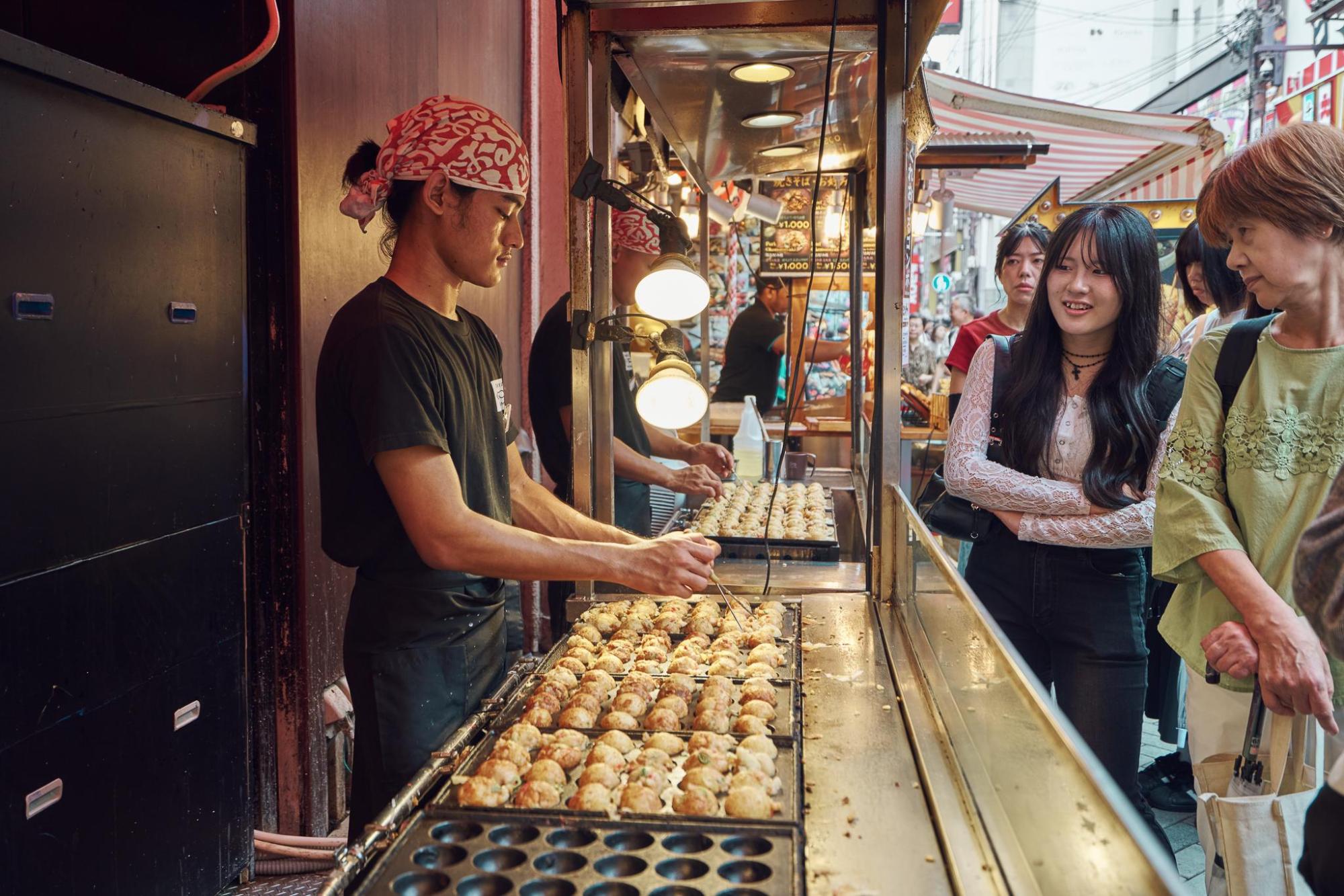 A street vendor cooking rows of takoyaki at a food stall