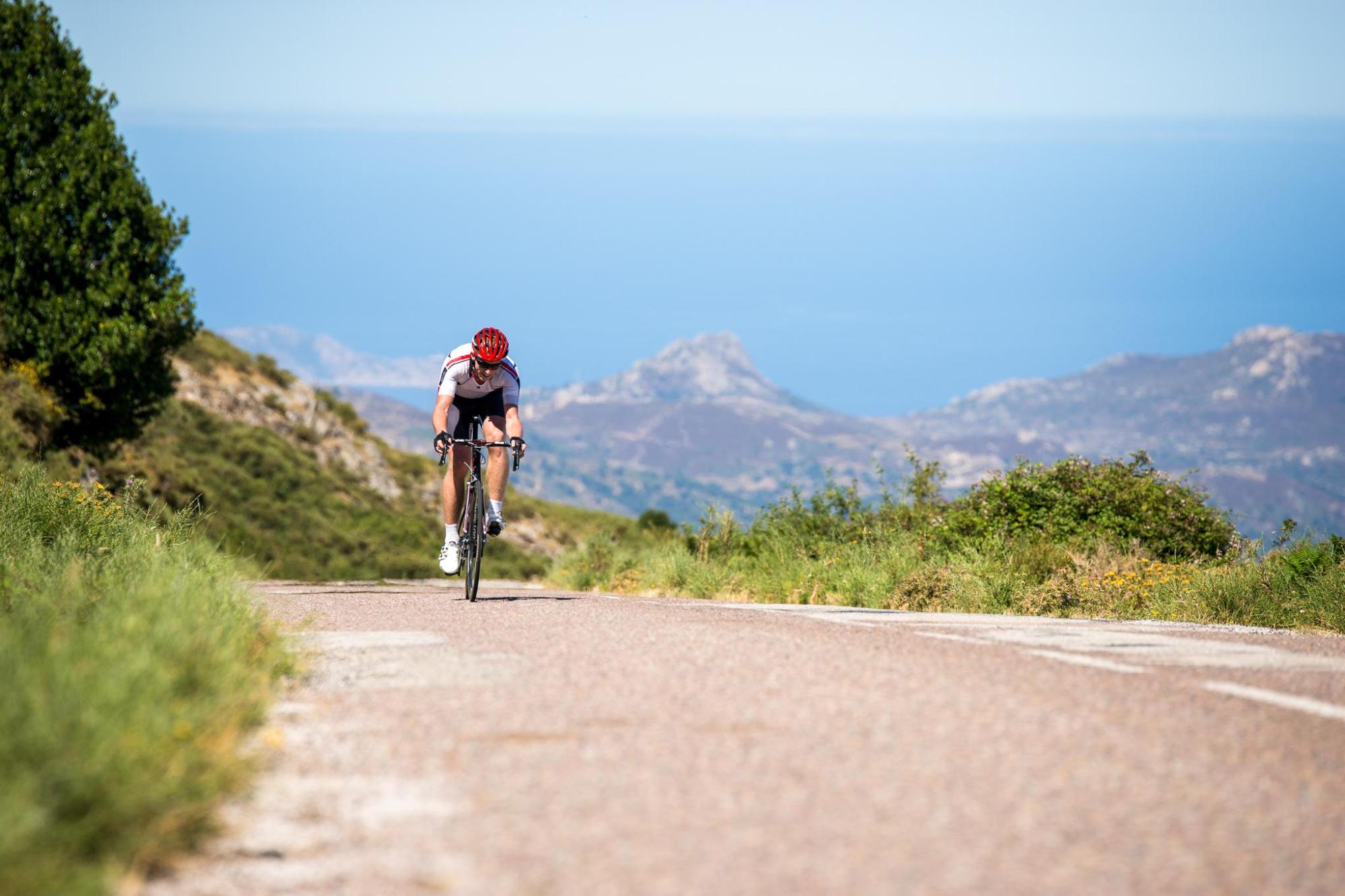 Cyclist riding along a mountain road with coastal views
