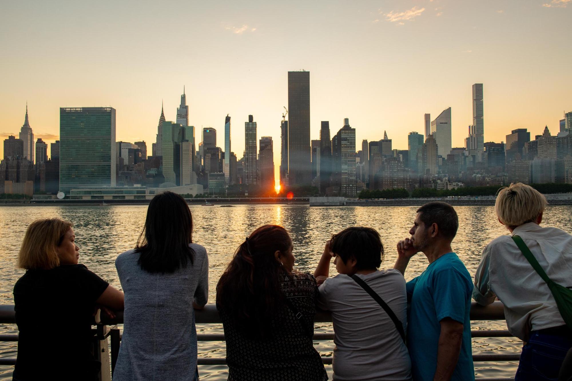 People overlooking a city skyline across the water at sunset