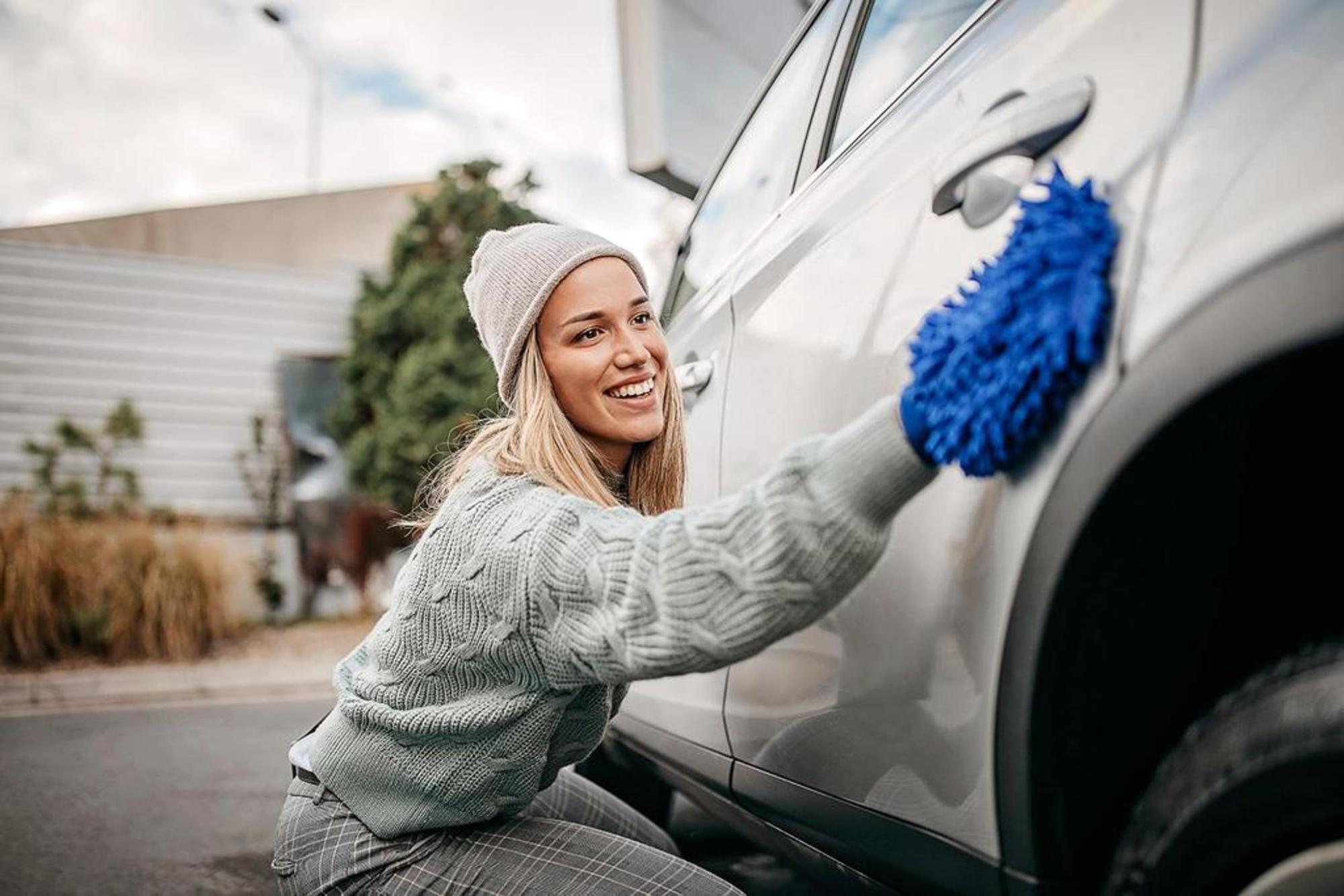 A woman smiling as she cleans her car