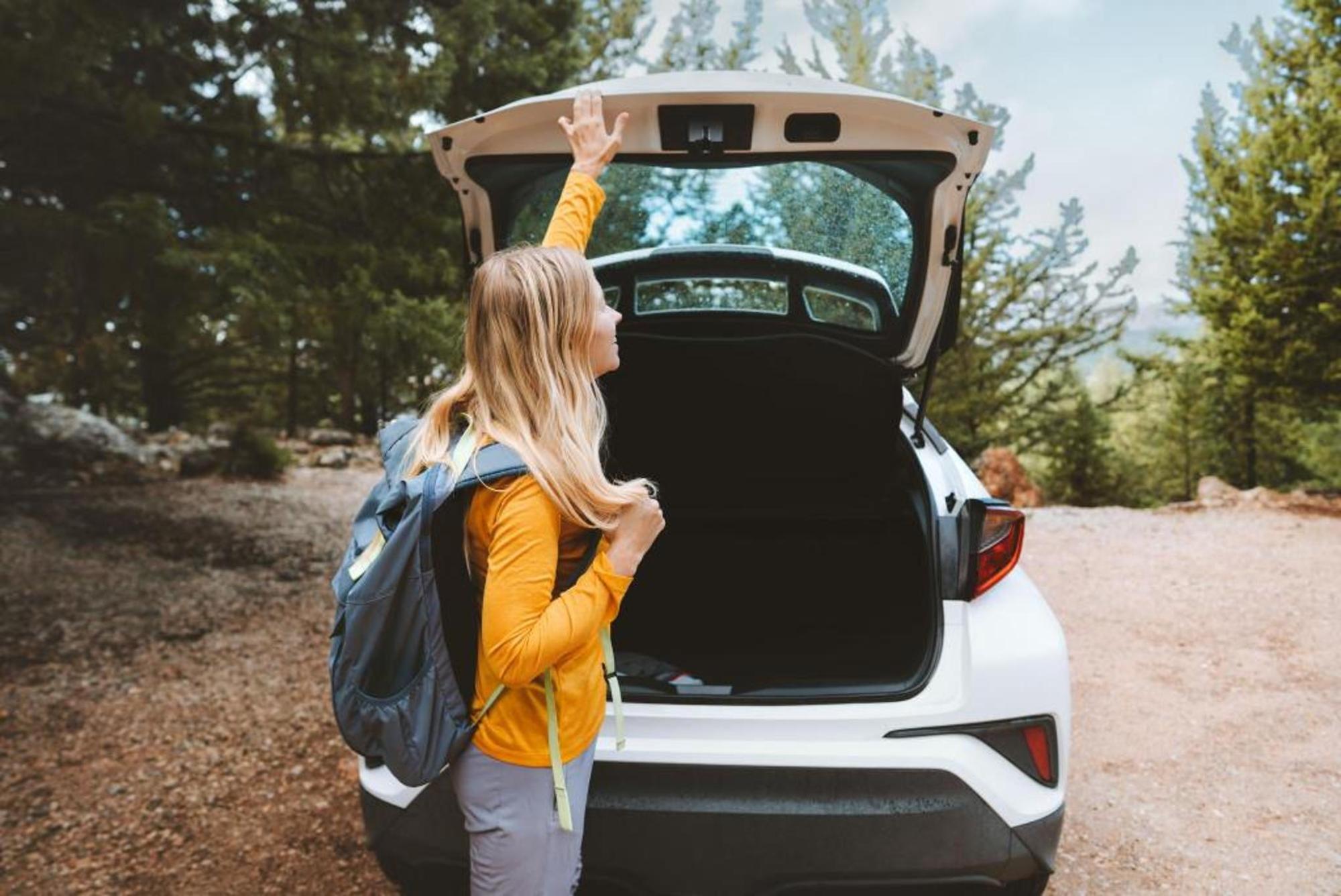 A woman wearing a backpack closing the trunk of her car