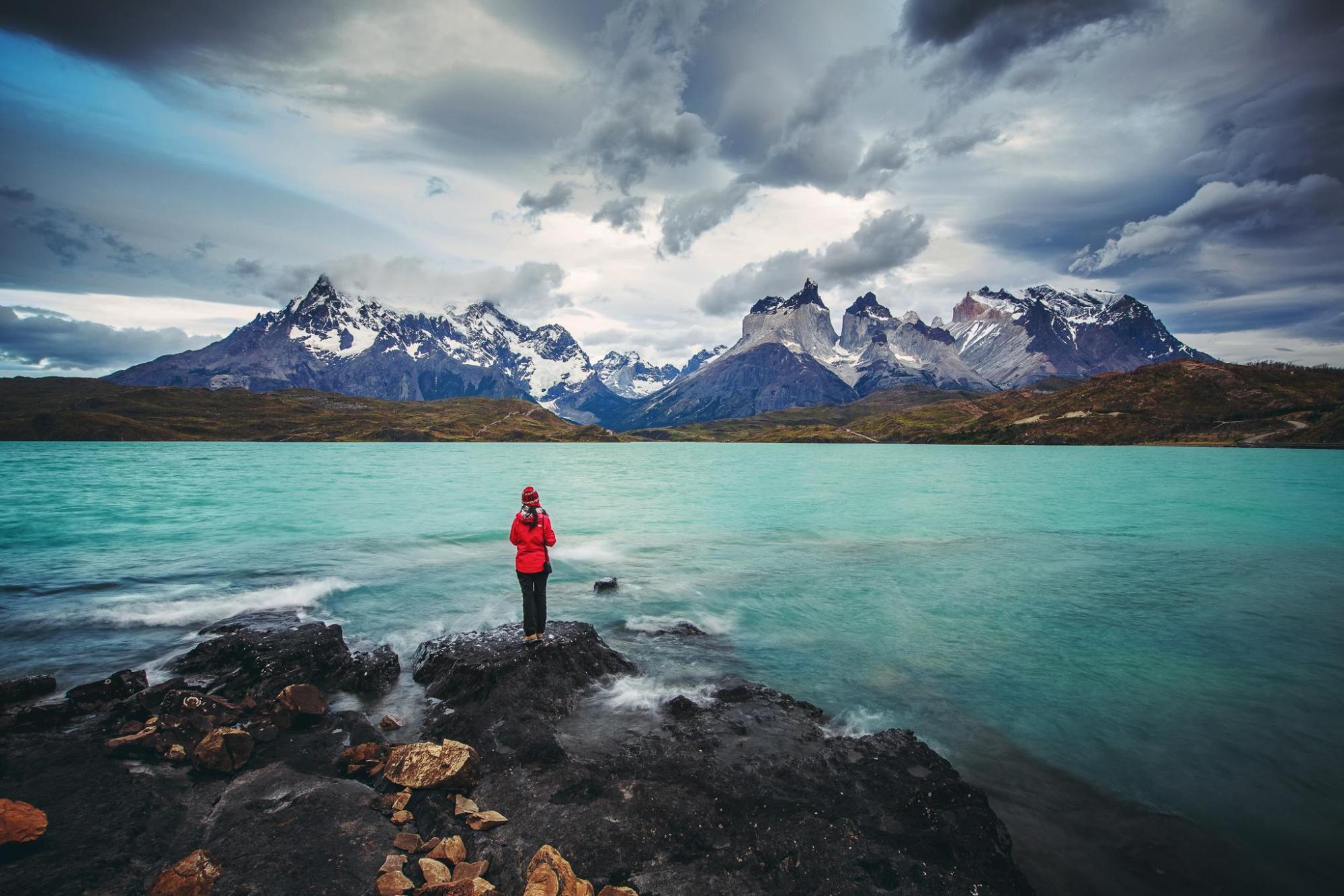 Traveler standing beside a lake with snow-capped mountains.