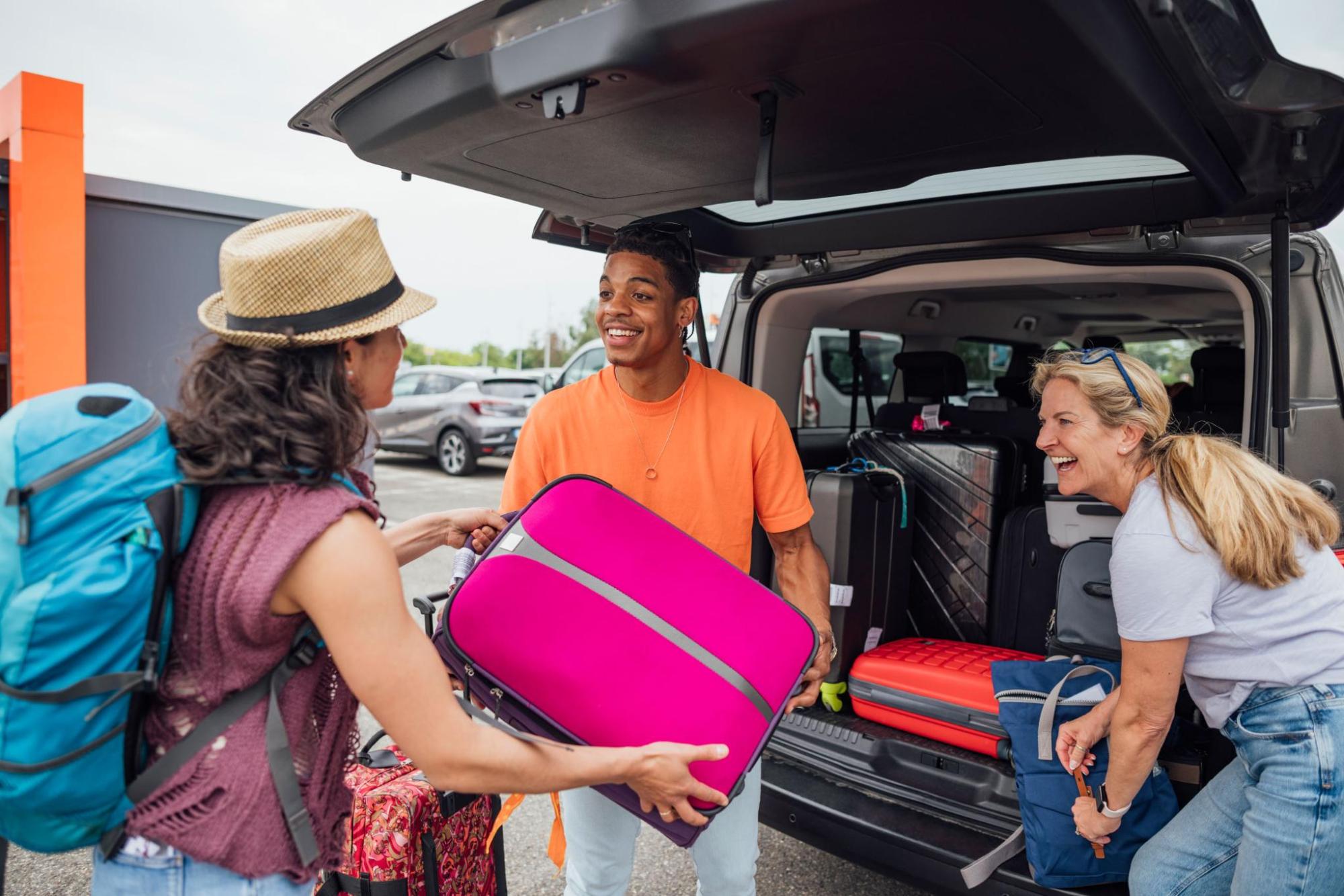 Three people packing bags into a car's trunk for travel.
