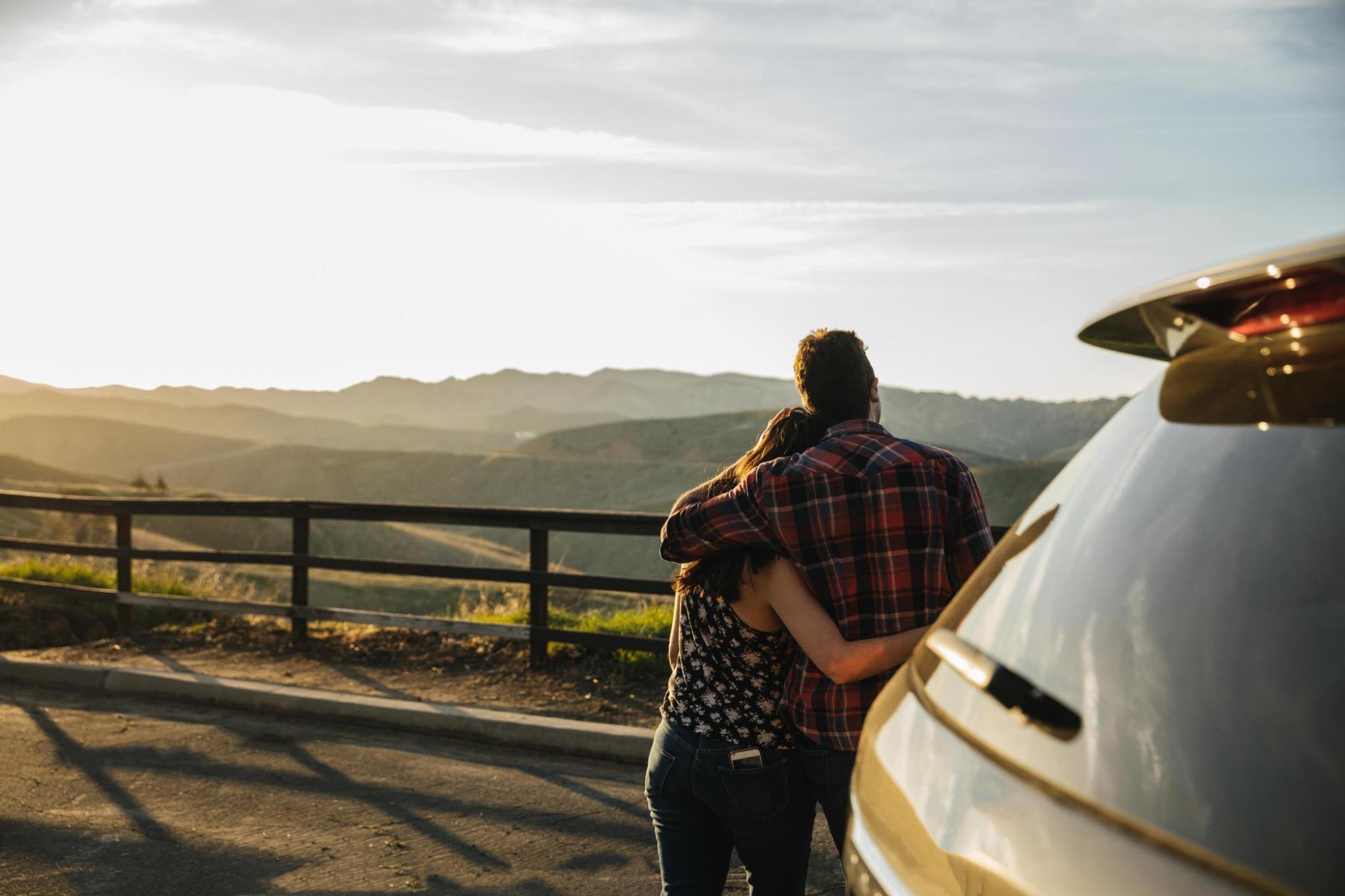 A couple cuddling by their car while watching sunset.