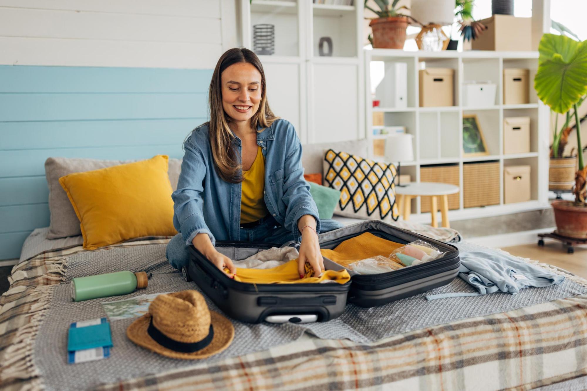 Traveller packing clothes into an open suitcase on a bed