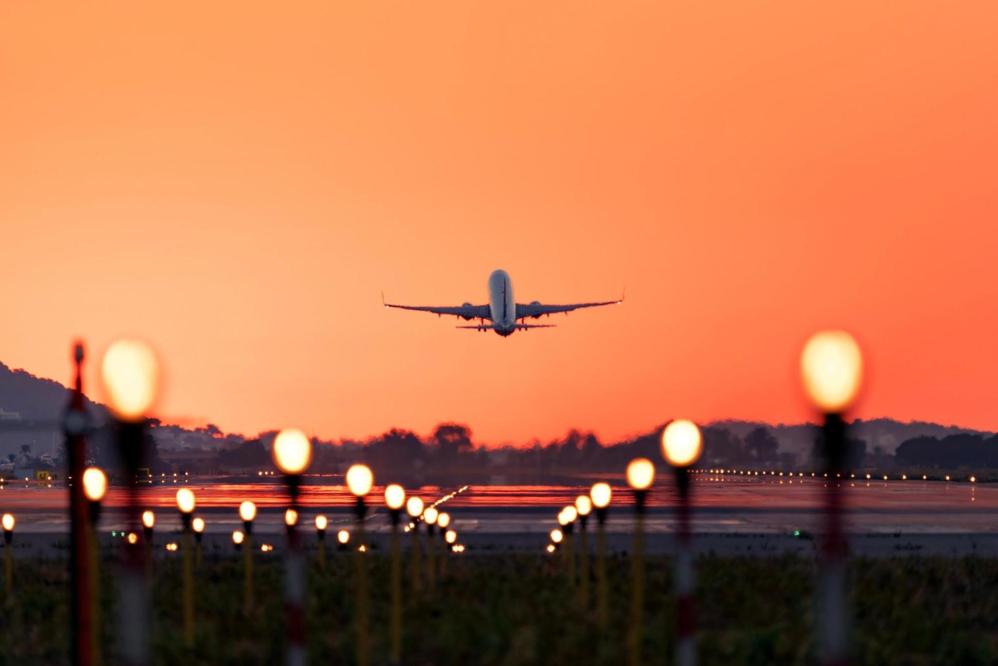 Airplane taking off at sunset above runway lights