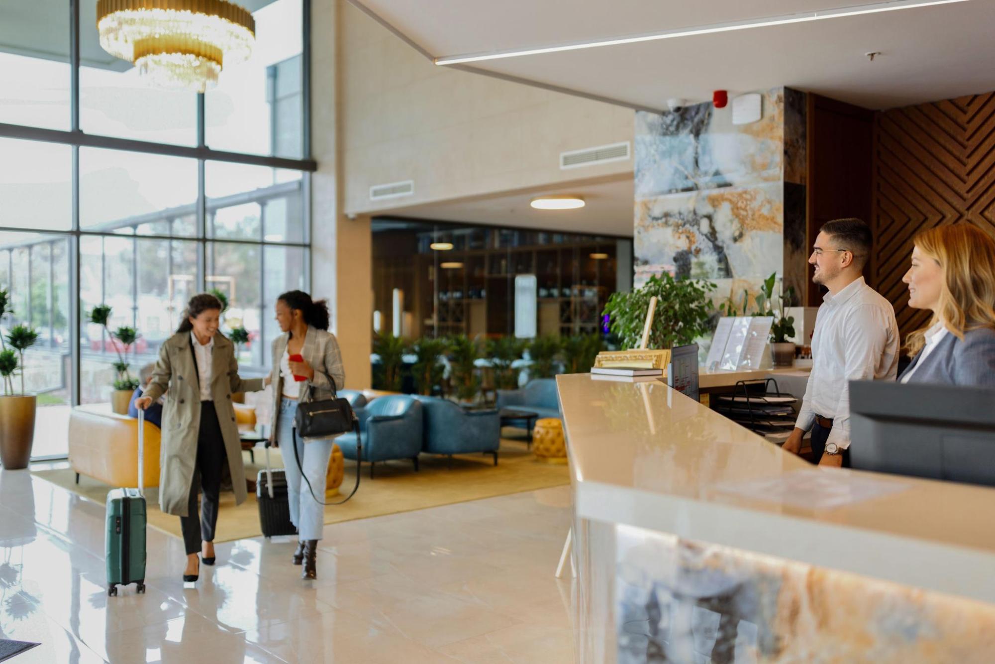Front desk area of a hotel, with guests and their suitcase.