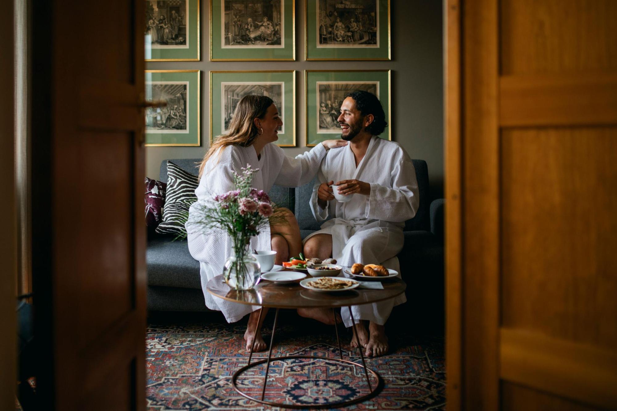 Couple in bathrobes sharing breakfast in a hotel suite
