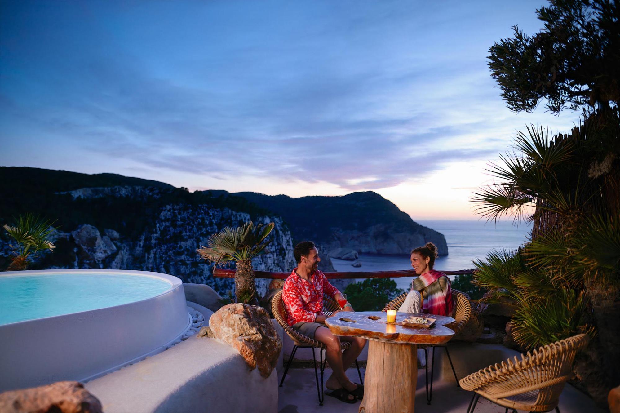 Couple dining outdoors beside a plunge pool with coastal views at dusk