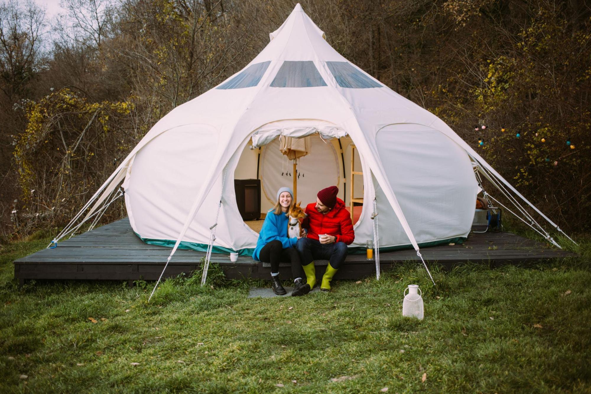 couple sitting with a dog outside a glamping tent 