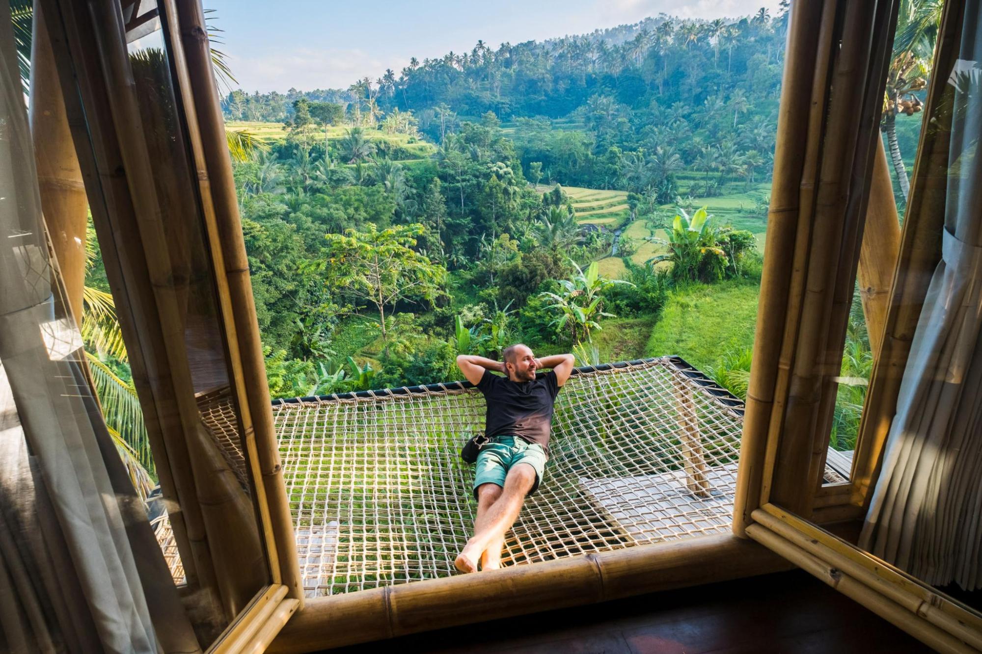 Man relaxing on a hammock-style terrace outside a bamboo villa, overlooking tropical trees