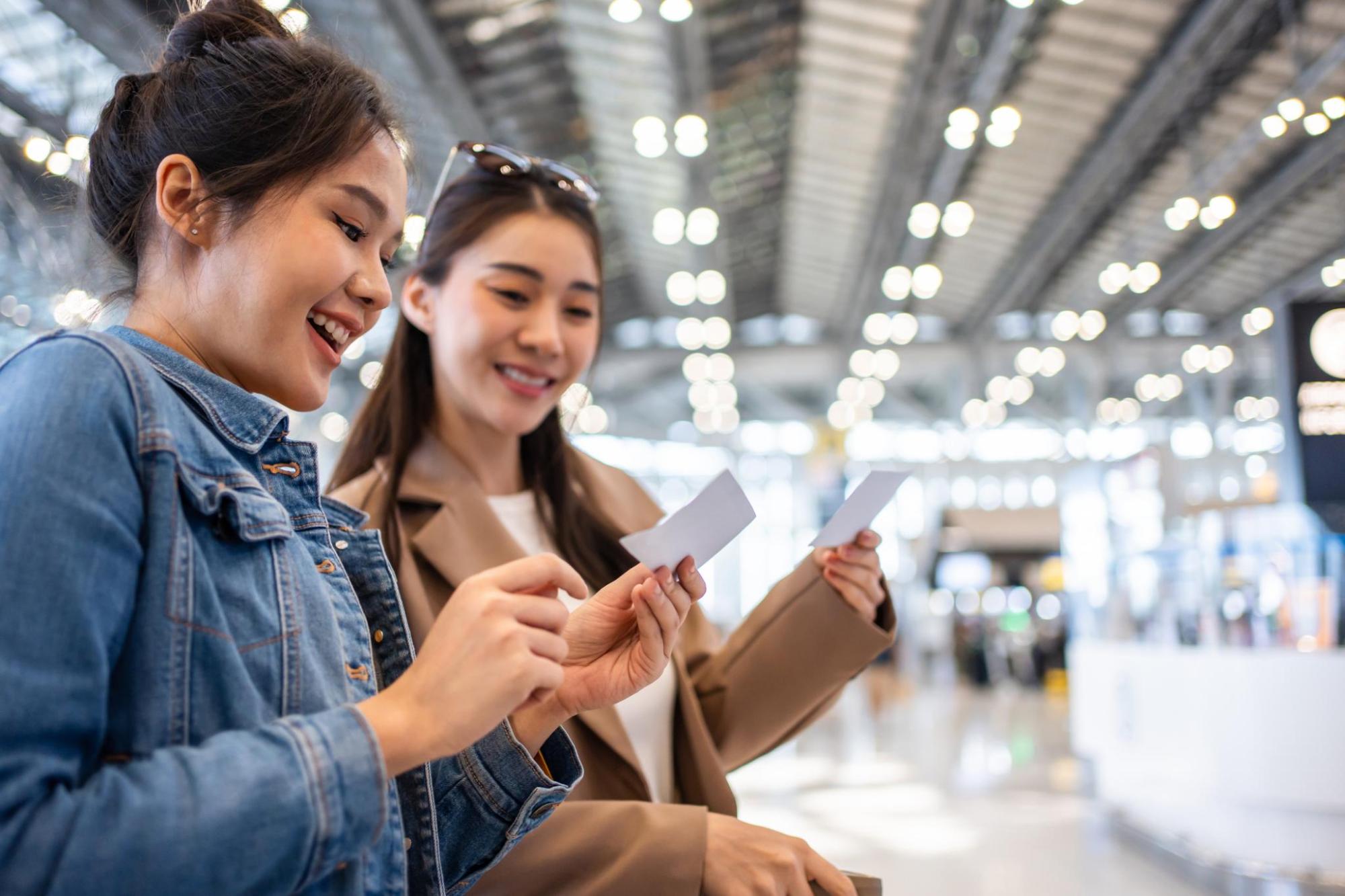 Two travellers smile while checking paper tickets inside a bright terminal building