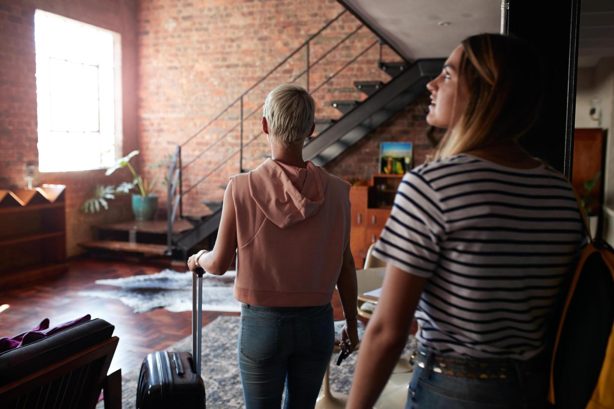 Two guests with suitcases enter a living room at their accommodation