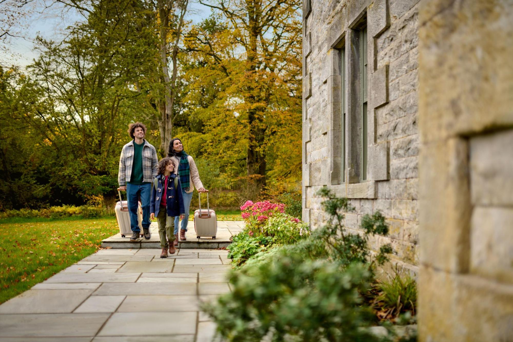 Two adults and a child with suitcases walking down a stone path towards a holiday home