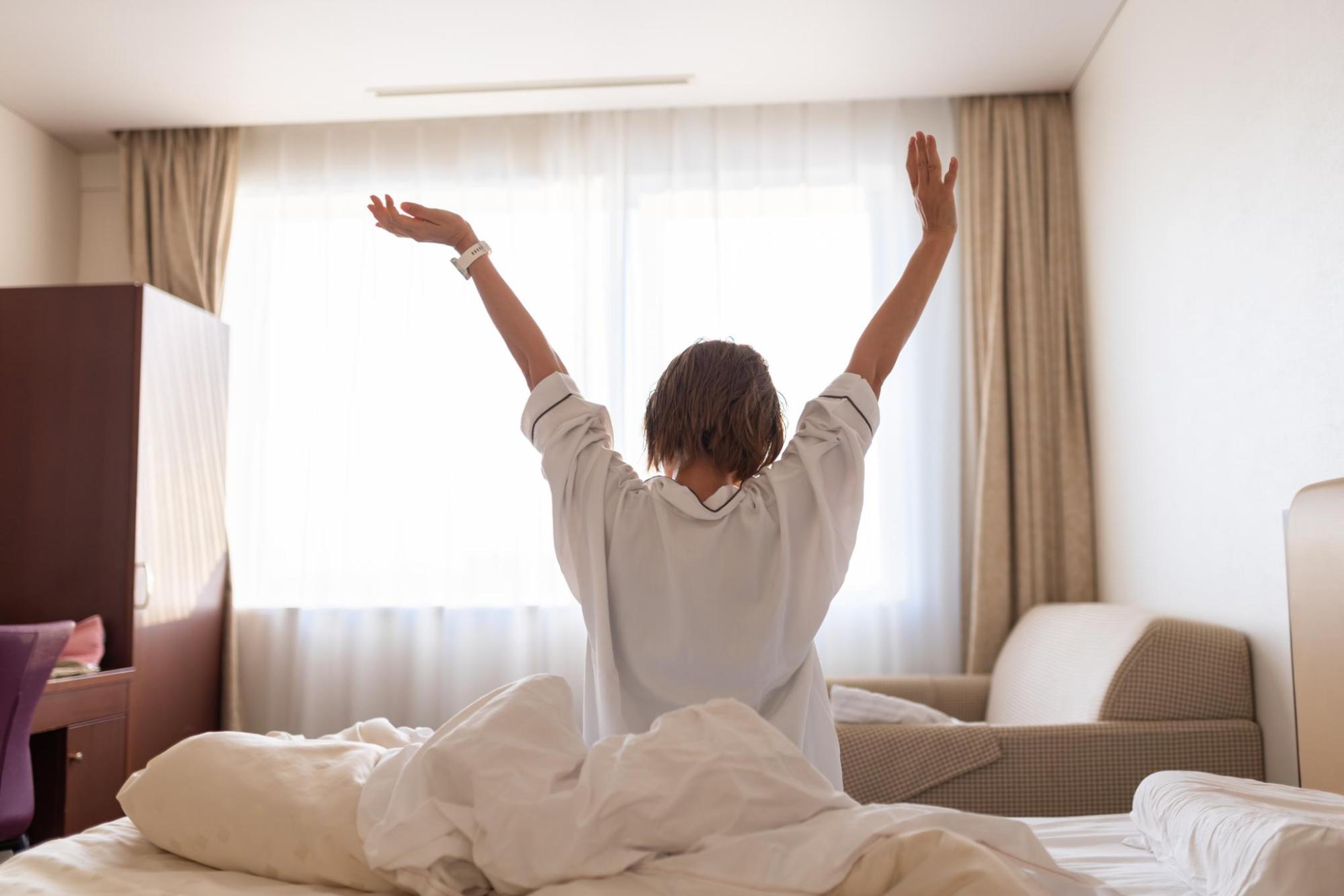 Hotel guest stretching on a bed in a bright room with sunlight through the curtains