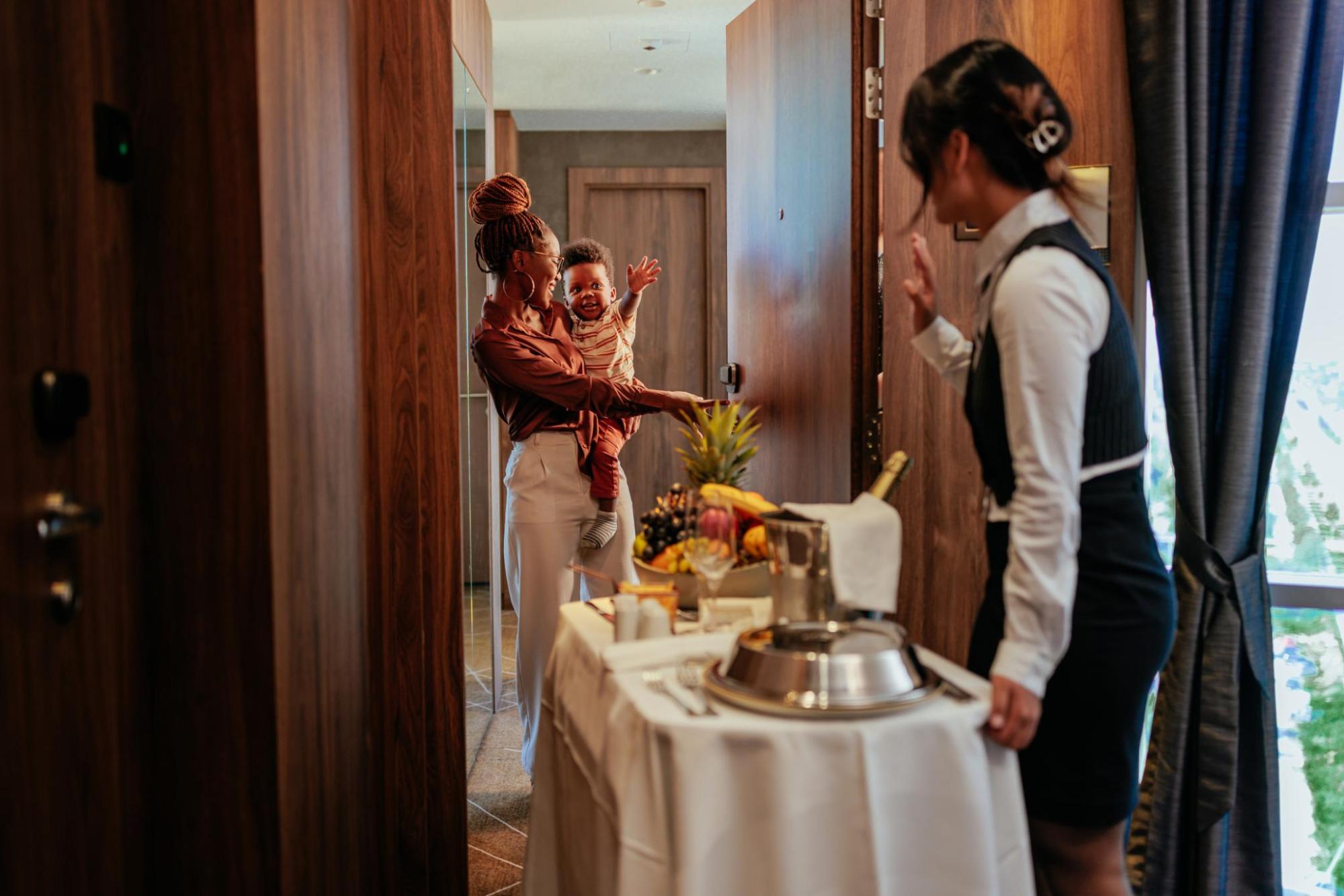 Woman holding a child opens a hotel room door to receive room service