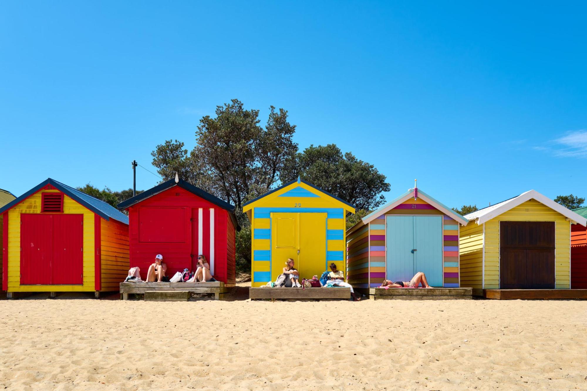 Brighton bathing boxes on a sandy beach under a clear blue sky