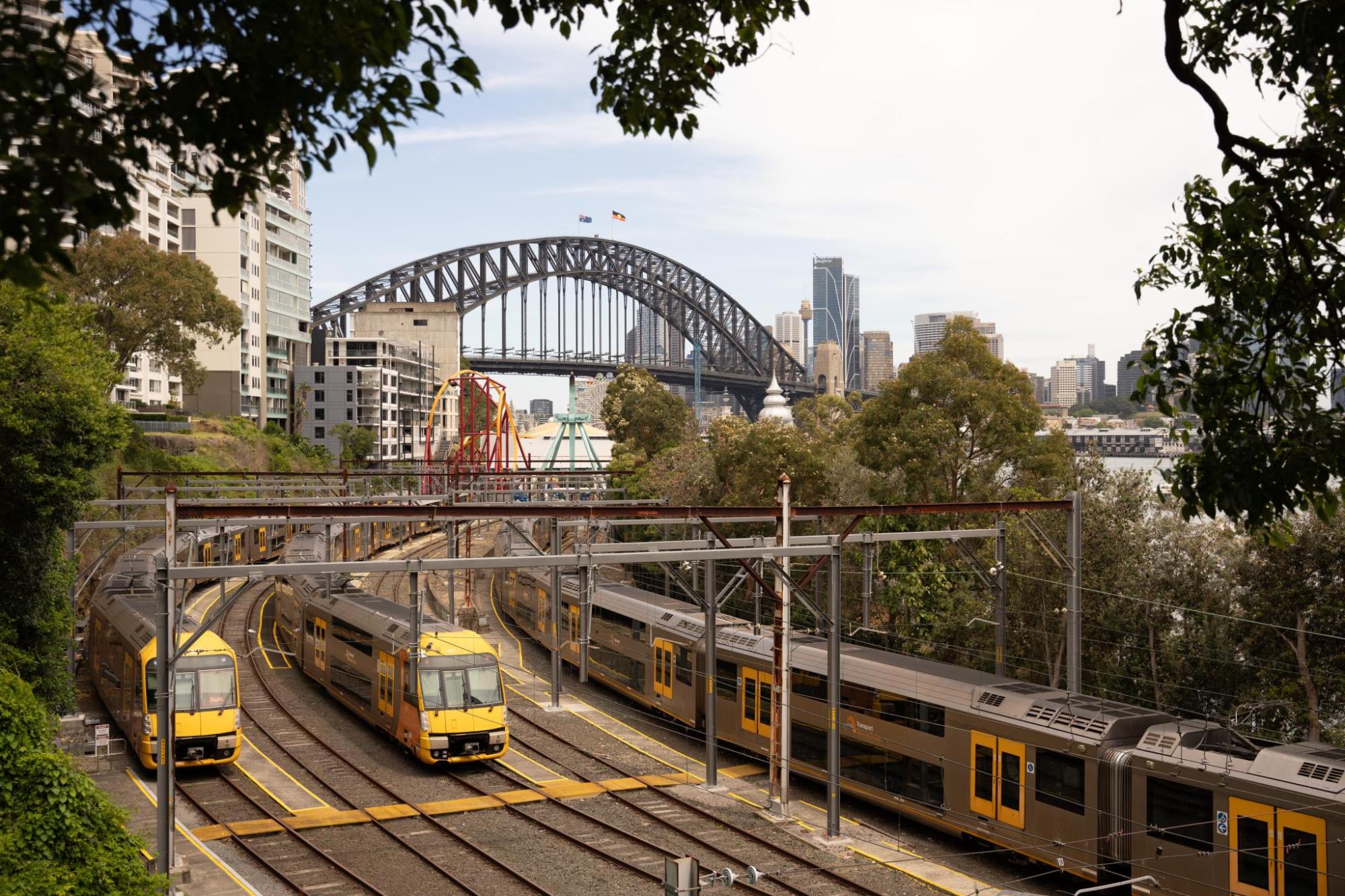 Three yellow trains on tracks near Sydney Harbour Bridge