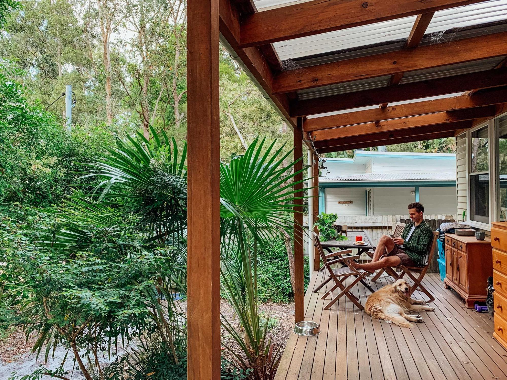 A man relaxes on a wooden deck with his dog by his side