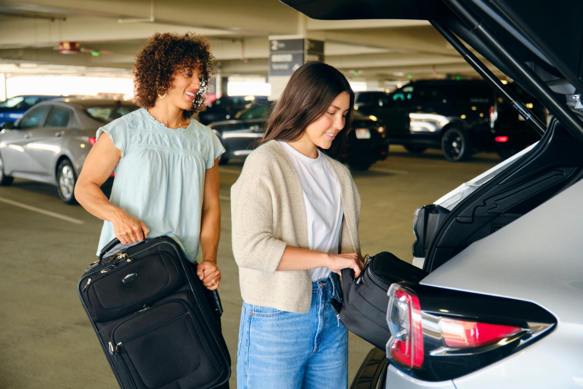 Two women loading luggage from the boot of a car in a car park