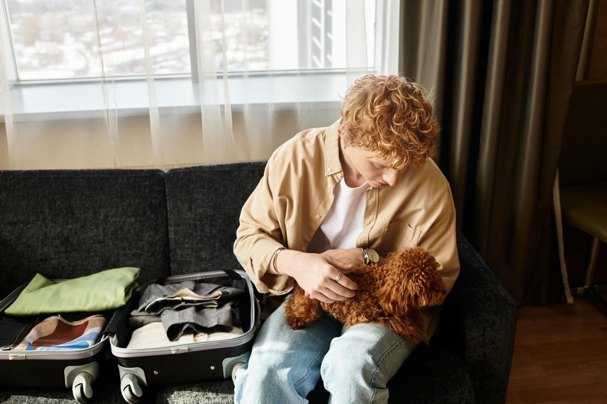 Guest with a small dog beside an open suitcase in a hotel room