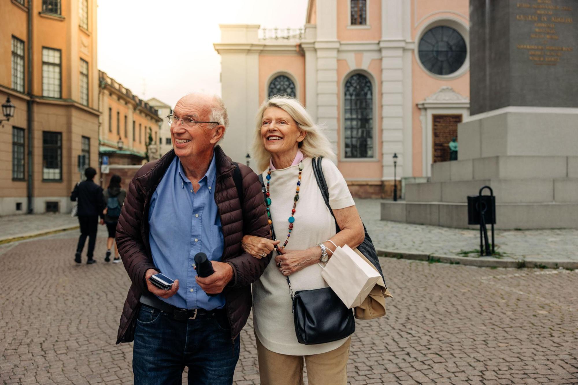Smiling couple walking through a cobbled square, with historic buildings and a church behind them