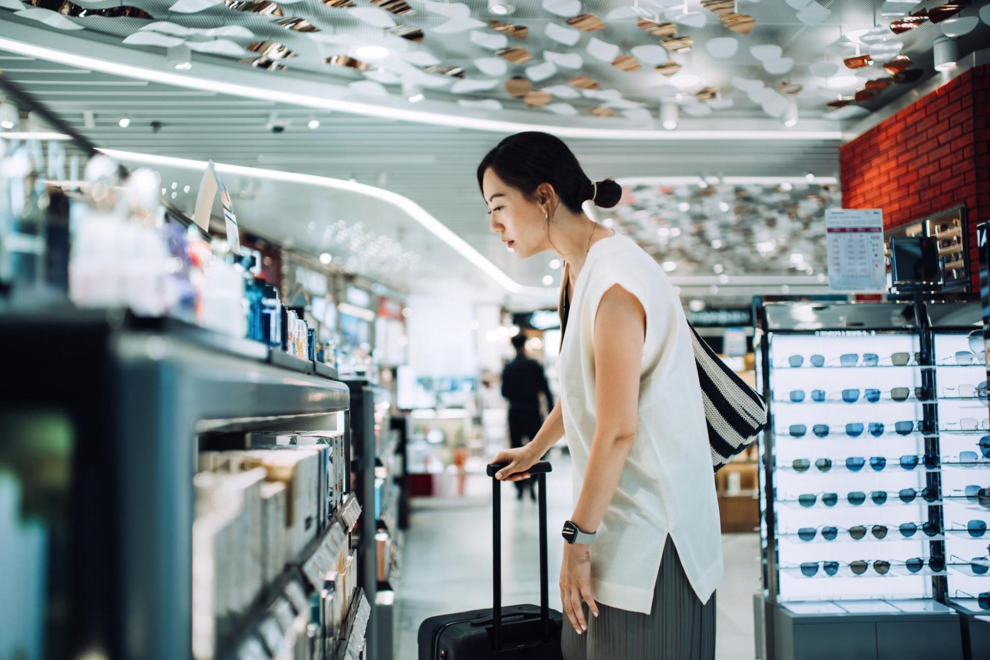 スーツケースをもった旅行者が空港の免税店で商品をチェックしている
