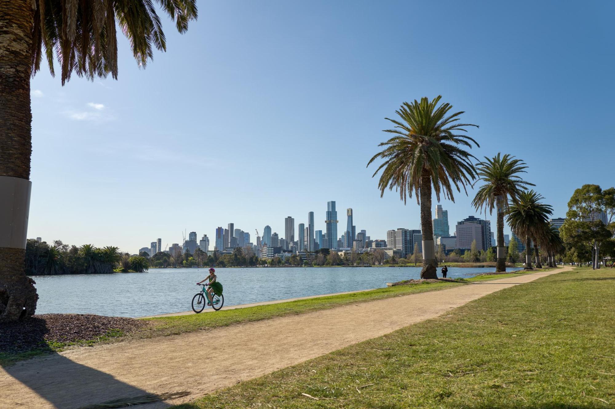 Cyclist riding beside Albert Park Lake with the Melbourne skyline in the background.