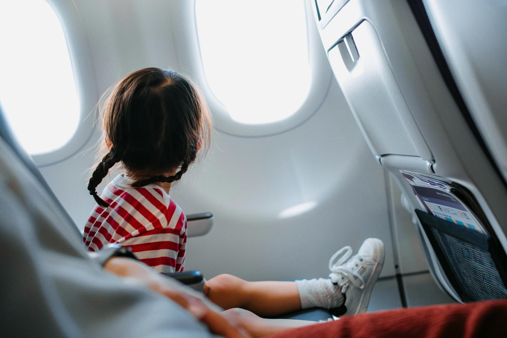 飛行機の座席に座り外を眺める子ども