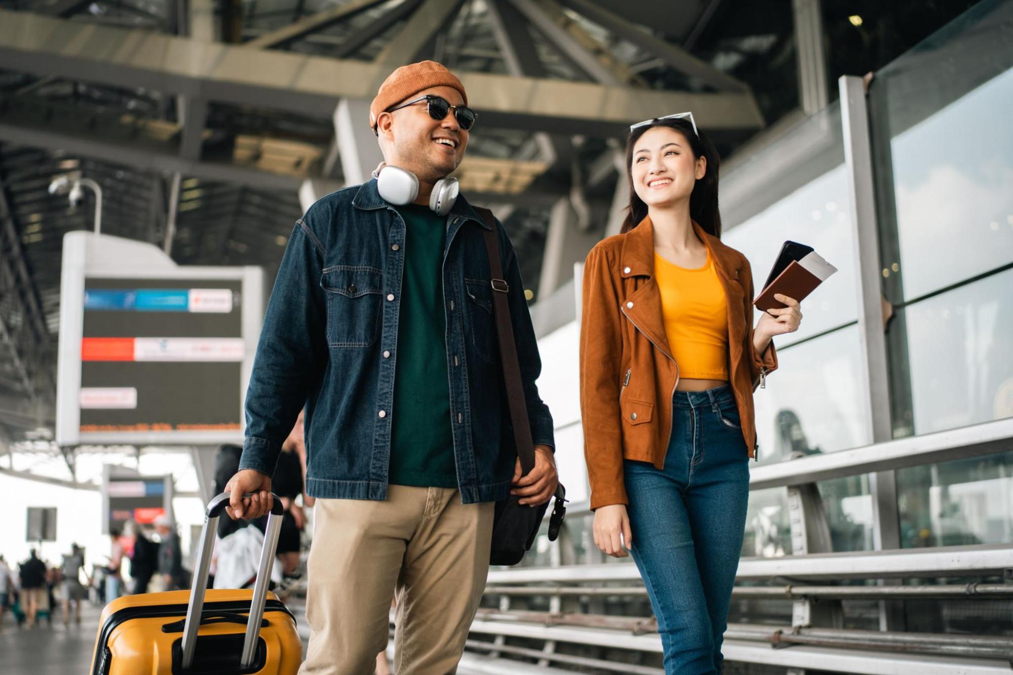 Deux voyageurs souriants avancent dans un aéroport avec leurs bagages et leurs documents de voyage