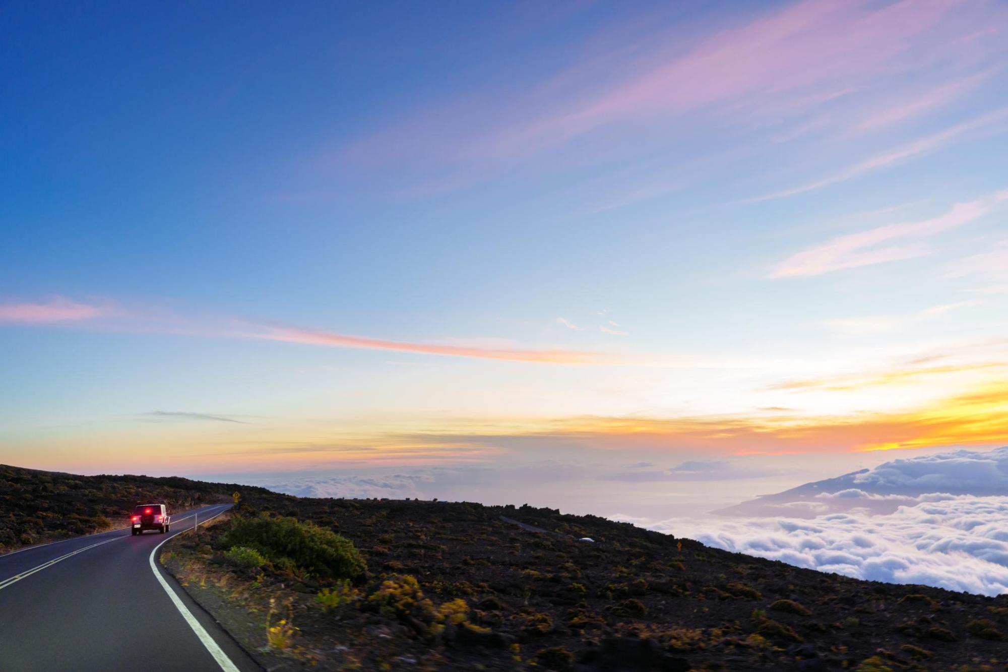 Voiture circulant sur une route désertique dans un paysage montagneux au coucher du soleil