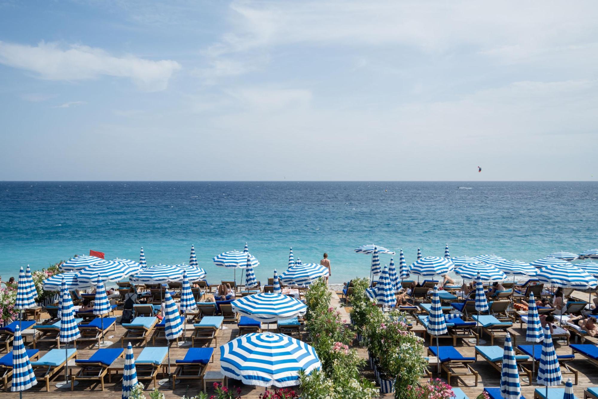 Plage bordée de parasols rayés bleus et blancs et de transats, face à la mer sous un ciel nuageux