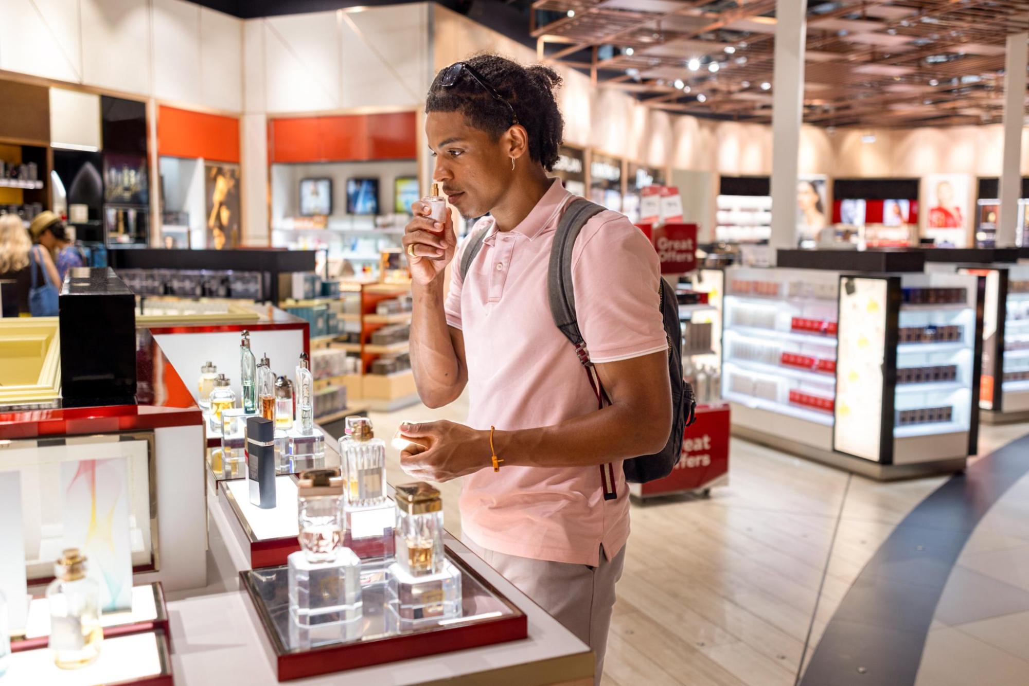 A man smelling perfume from a test bottle inside a duty-free shop