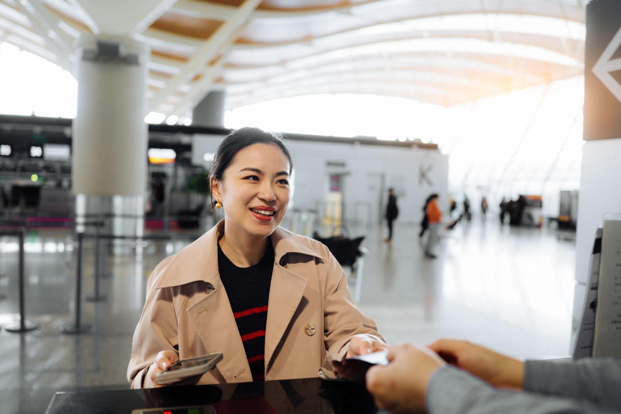 Une femme souriante présente ses documents au comptoir d’un aéroport