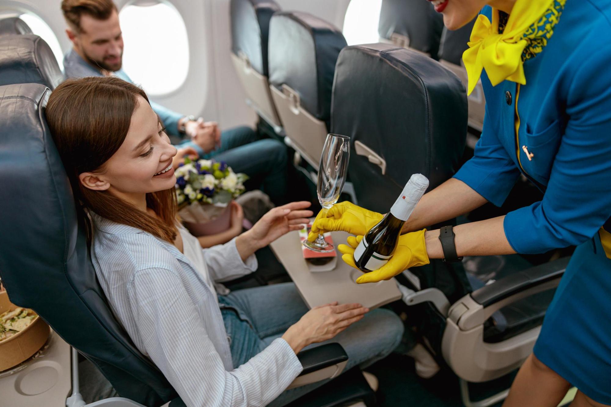 Flight attendant serving a drink to a smiling passenger on a plane