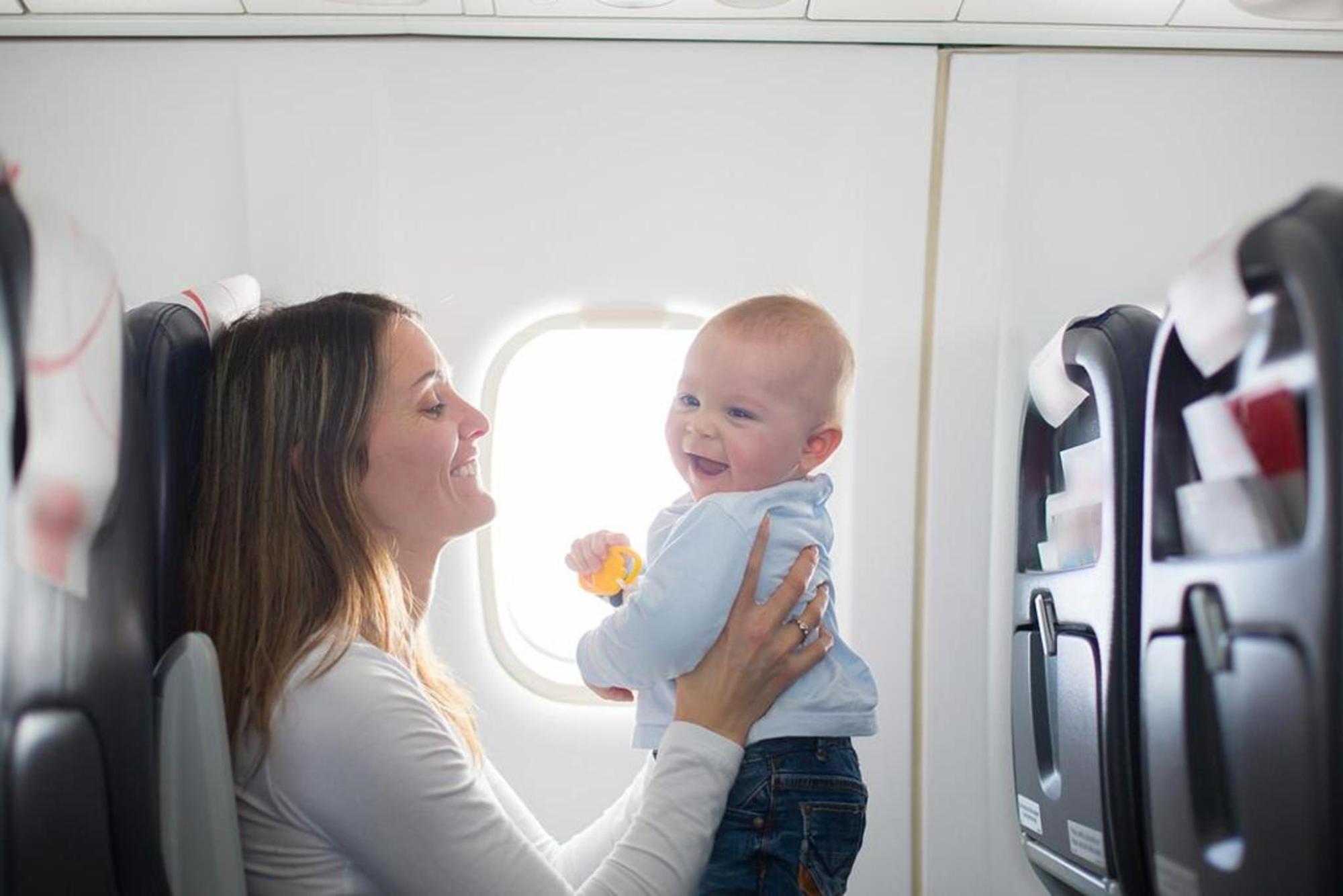 Eine Frau hält ein Baby vor einem Fenster in der Kabine eines Passagierflugzeugs.