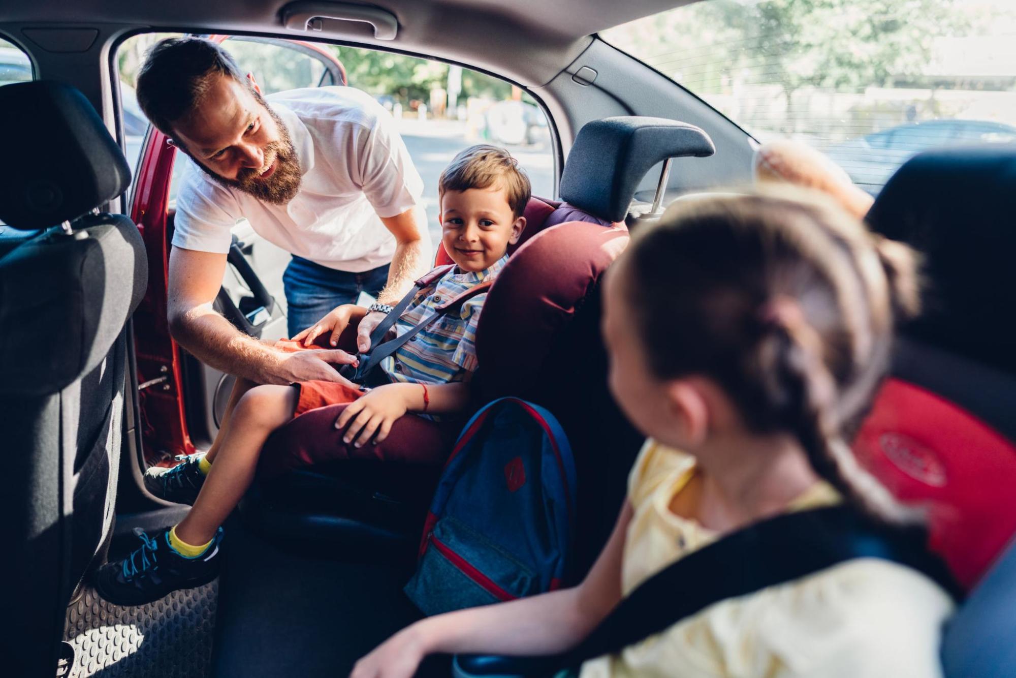 A man buckles a kid into a car seat in the back of a vehicle.