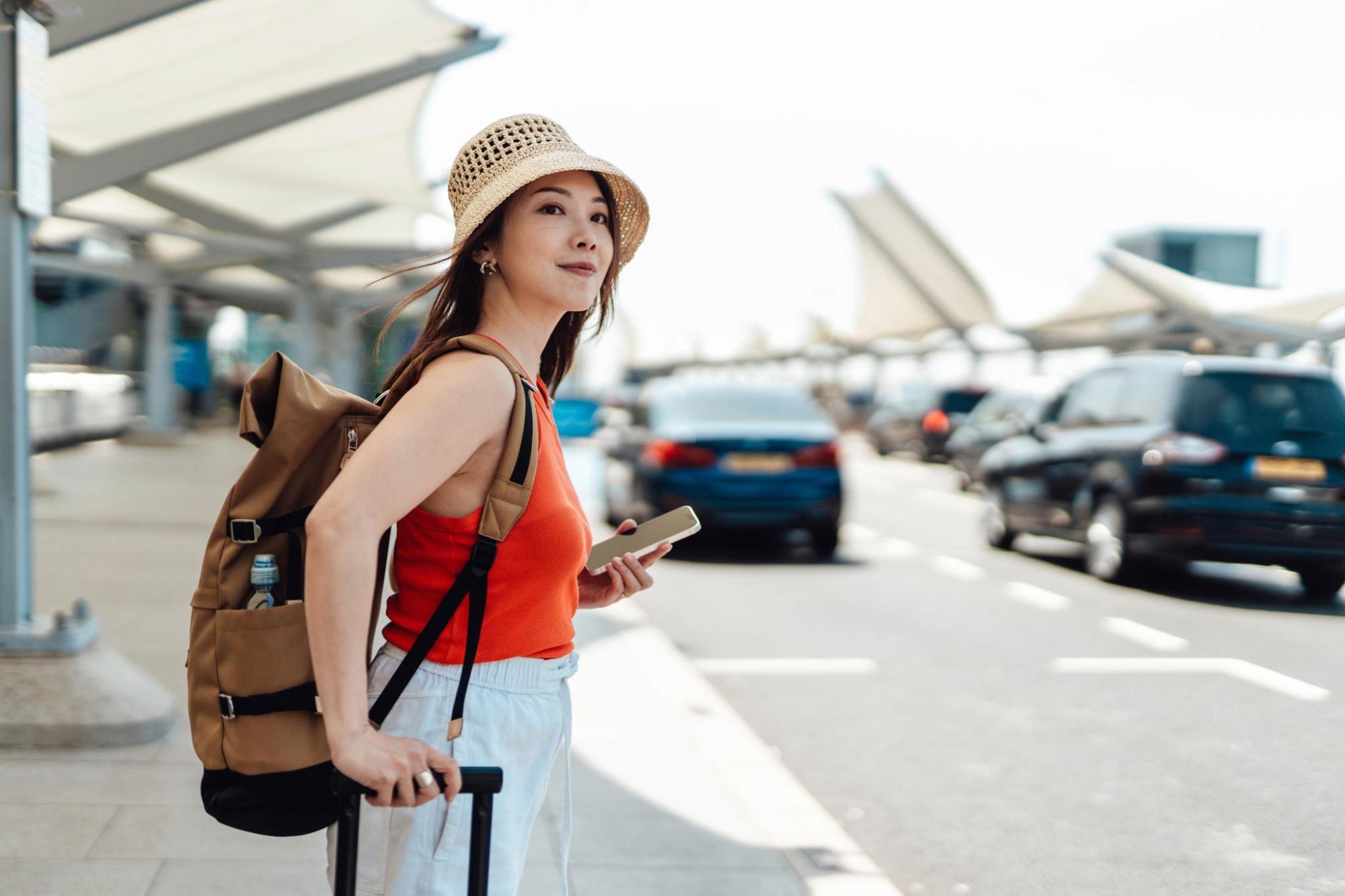Une femme, équipée d'un sac à dos et d'un chapeau, se tenant devant une voiture, à l'aéroport