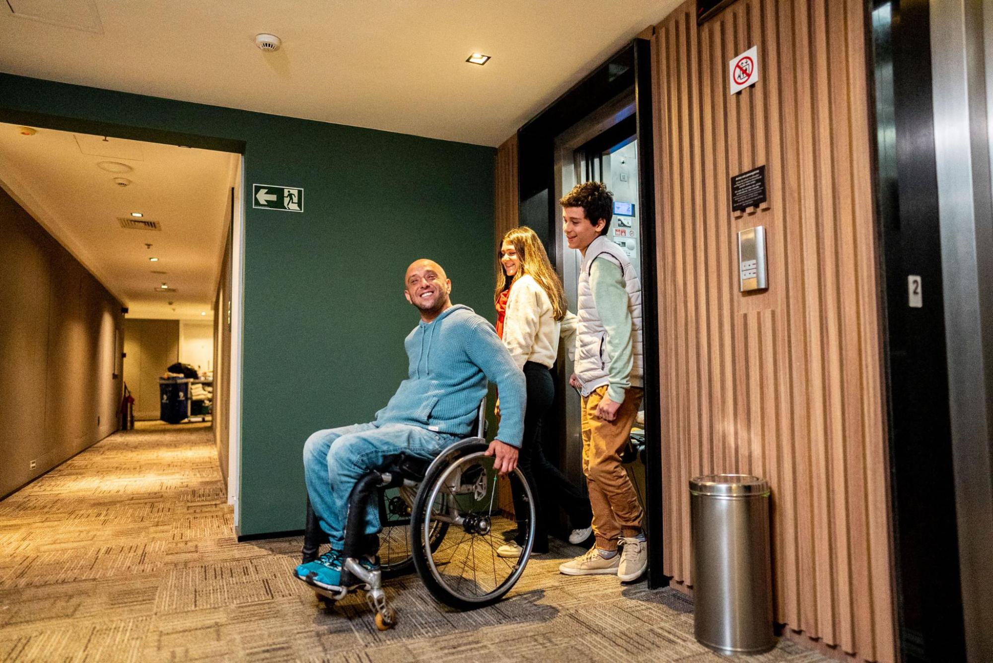 A wheelchair user leaves an elevator with help from two people in a corridor