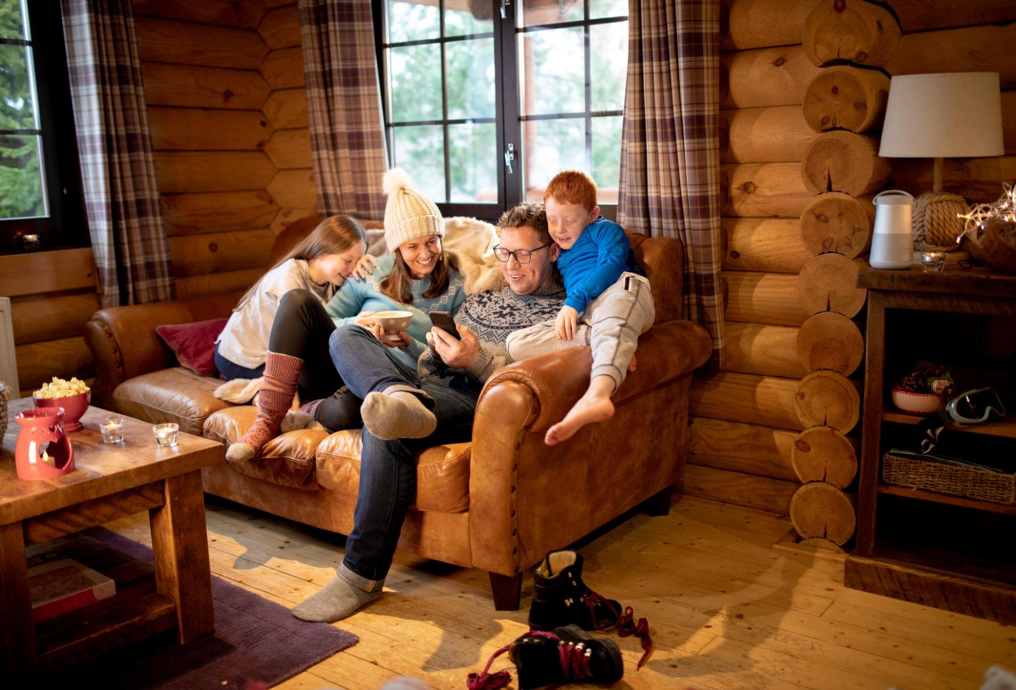 Une famille assise sur un canapé dans un chalet en rondins, dans une ambiance rustique
