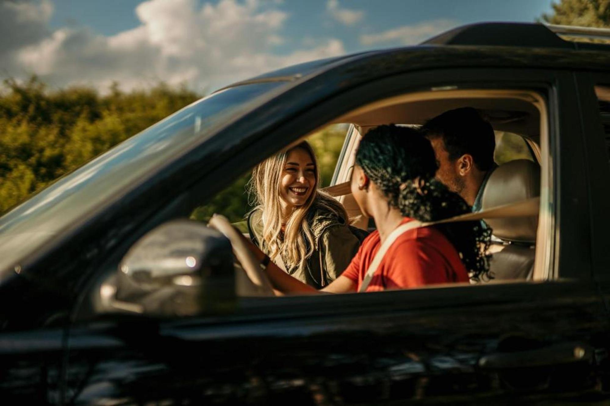 Two women and a man in the backseat laugh in a rental car