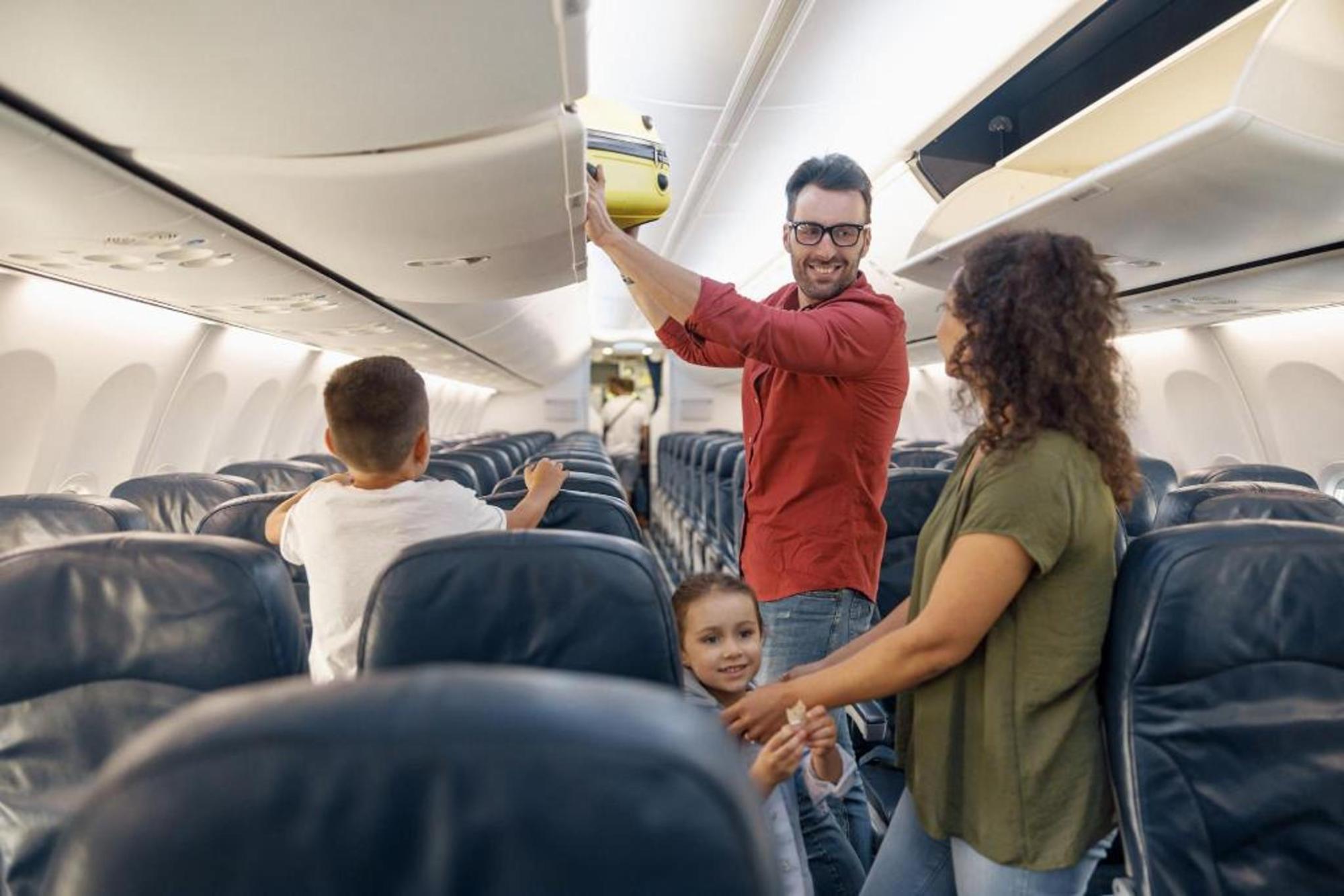 A man smiling as he places his bag into the overhead bins
